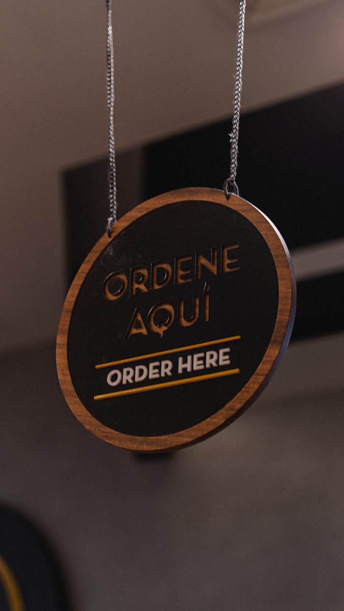 Hanging circular sign with 'Ordene Aquí, Order Here' in a modern cafe setting.