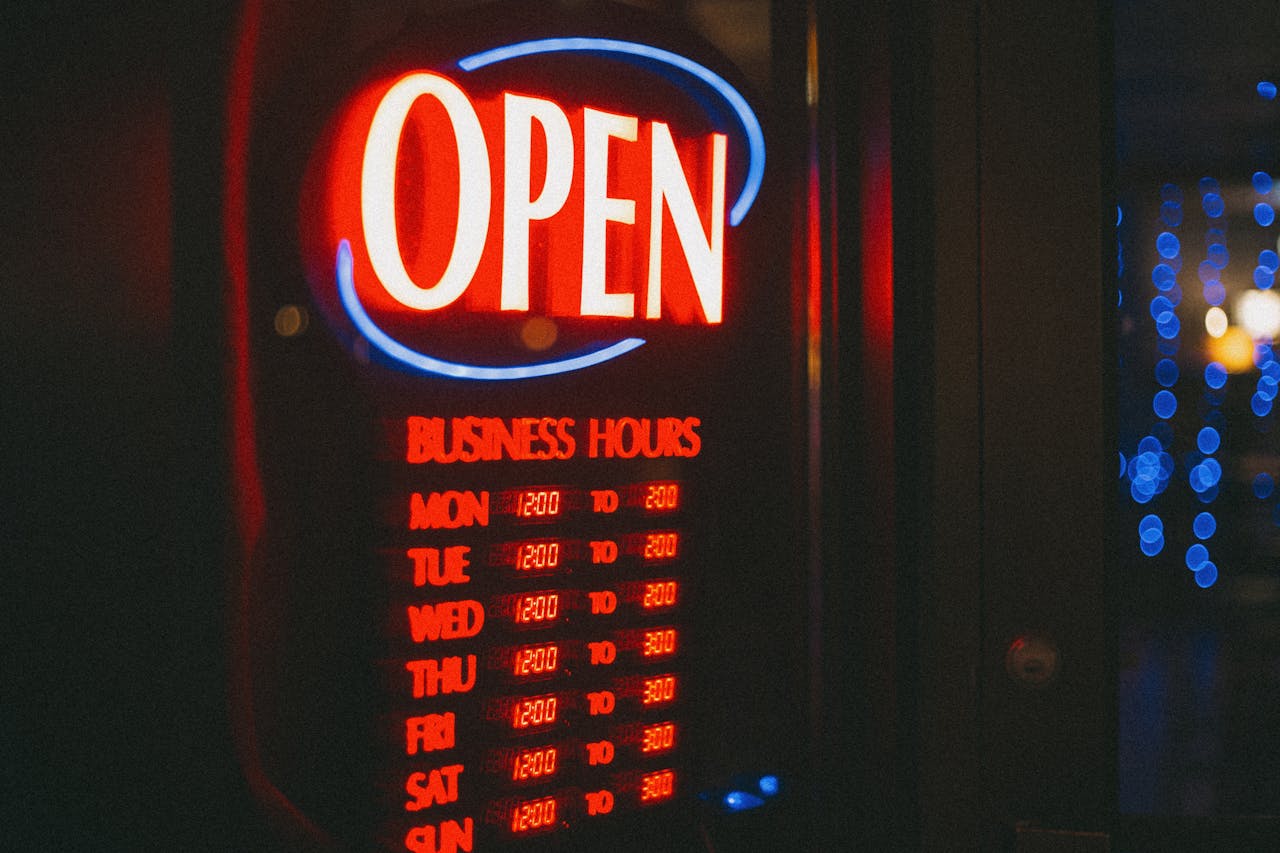 Bright neon open sign displaying business hours, glowing against a dark background.